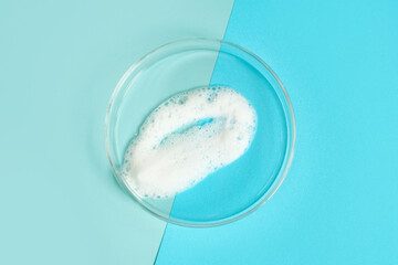 Smear of facial cleansing foam in a petri dish on blue background close-up.