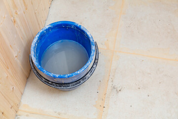 A blue bucket with a white substance in it is sitting on a tile floor