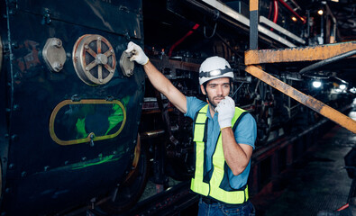 Male engineer worker maintenance locomotive engine wearing safety uniform, helmet and gloves in locomotive repair garage. Maintenance cycle concept.