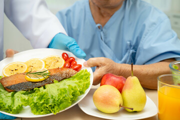 Asian elderly woman patient eating salmon stake and vegetable salad for healthy food in hospital.