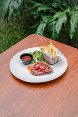 Beef Steak with French Fries, Fresh Salad, and Sauce on a White Plate Served Al Fresco on a Wooden Table.