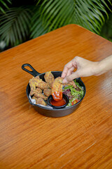 Hand Put Chicken Wings with Savory Sauce and Fresh Salad Served on a Skillet, Placed on a Wooden Table.