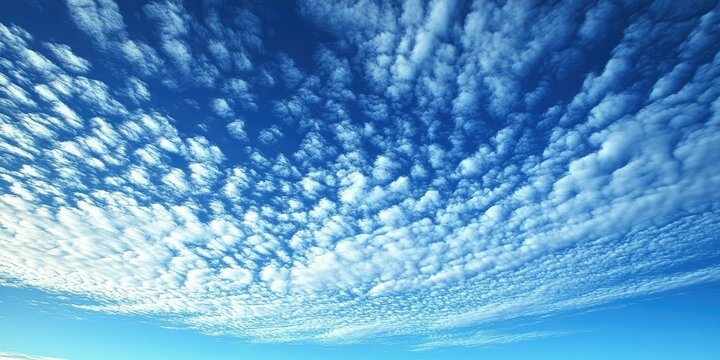 Scattered white cirrocumulus stratiformis clouds against a vibrant blue sky with a varying texture and density creating a serene atmosphere.