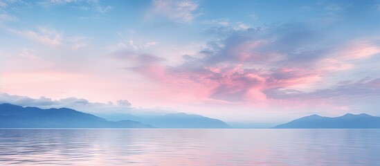 Fototapeta premium Serene twilight sky with soft pink and blue hues illuminating clouds over tranquil azure water reflecting distant mountains