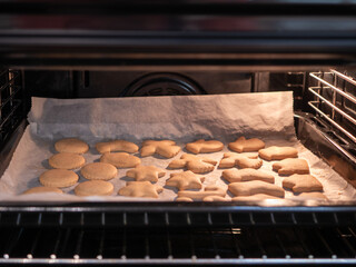 Gingerbread cookies baking in an electric oven. The cookies, cut into various festive shapes, are...