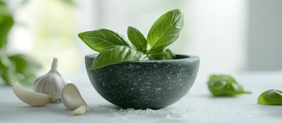 Obraz premium Fresh basil leaves and garlic cloves in a black stone mortar on a light table with a blurred green background highlighting culinary creativity
