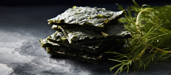 Crispy nori seaweed sheets stacked on a dark grey surface with fresh herbs in the background showcasing a healthy Japanese snack option