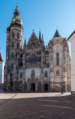 Naklejka premium The image shows St. Elisabeth Cathedral in Košice, Slovakia, a stunning Gothic structure with intricate stone detailing, pointed arches, and towering spires. The cathedral stands against a clear blue 