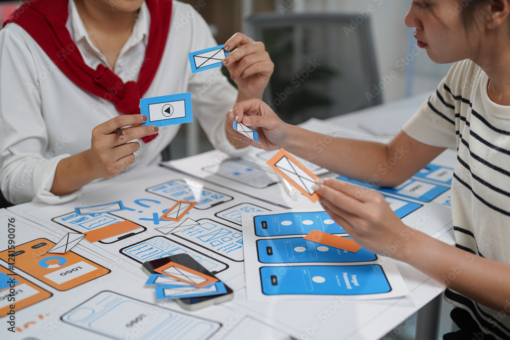 Poster two female ui/ux designers collaborating on a new mobile application, arranging icons on the app's w