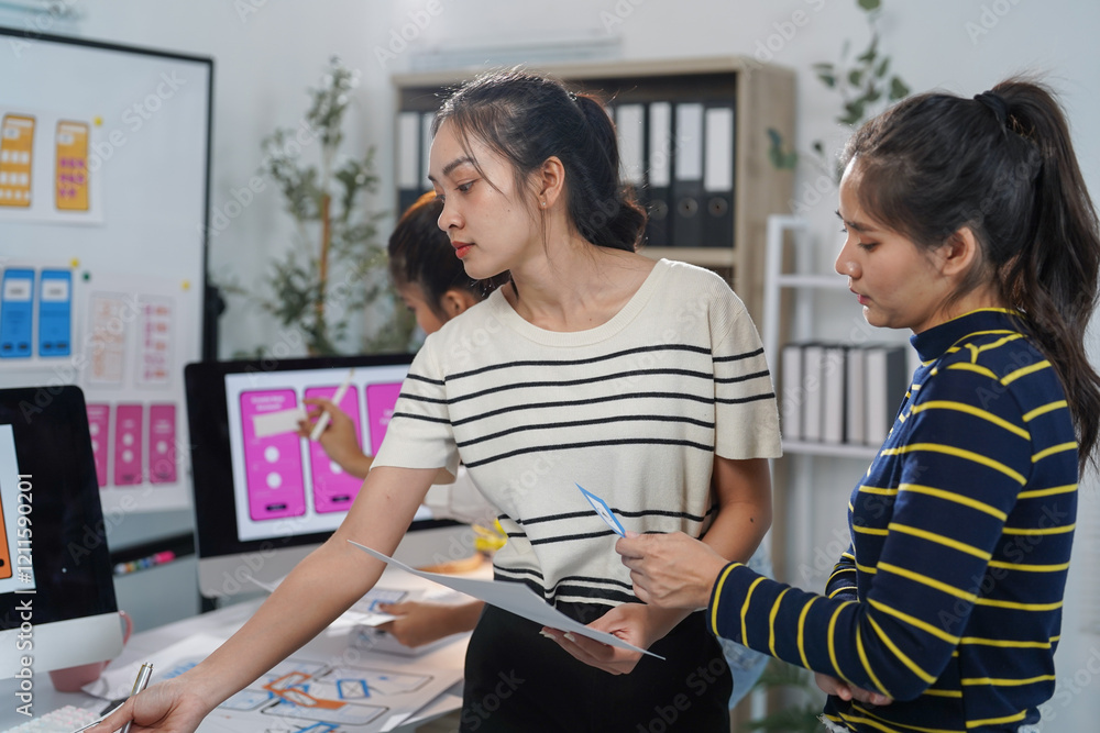 Poster asian female ux designers collaborating in an office, analyzing mobile app interface wireframes and 