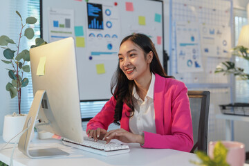 Young asian businesswoman smiling while working at a desktop computer in a modern office, with...