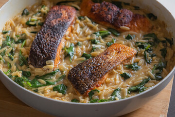 Close-up of a cooked salmon filet with orzo pasta and spinach in a white pan, showcasing a healthy and delicious meal