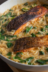 Close-up of a cooked salmon filet with orzo pasta and spinach in a white pan, showcasing a healthy and delicious meal