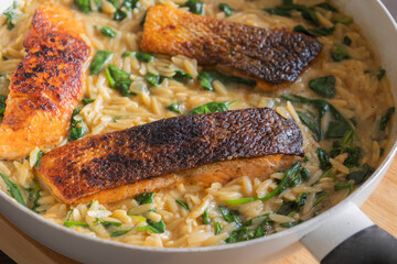 Close-up of a cooked salmon filet with orzo pasta and spinach in a white pan, showcasing a healthy and delicious meal