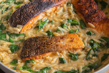 Close-up of a cooked salmon filet with orzo pasta and spinach in a white pan, showcasing a healthy and delicious meal
