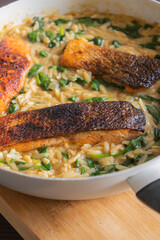 Close-up of a cooked salmon filet with orzo pasta and spinach in a white pan, showcasing a healthy and delicious meal