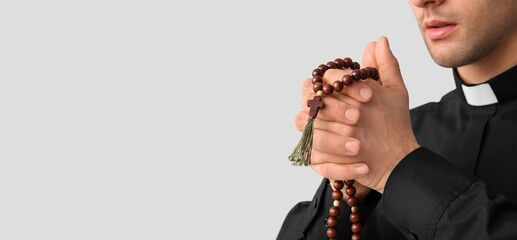 Young priest praying with beads on light background with space for text, closeup