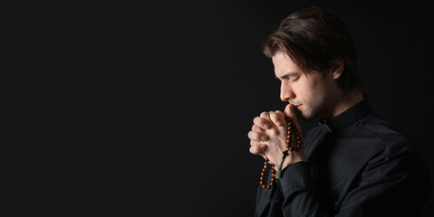 Young priest praying with beads on dark background, closeup