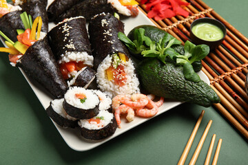 Plate with tasty sushi cones, rolls, shrimps, avocado and lambs lettuce on green background, closeup