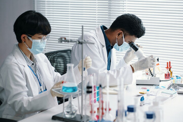 Scientists conducting experiments while wearing lab coats and protective masks in laboratory...