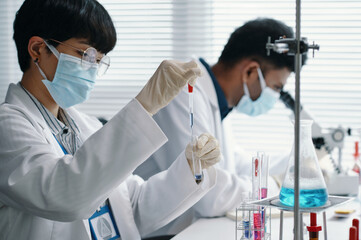 Researchers conducting experiments inside modern laboratory, wearing lab coats and protective...