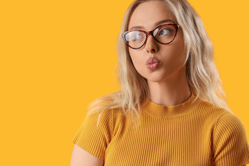 Young woman in stylish eyeglasses blowing kiss on orange background, closeup