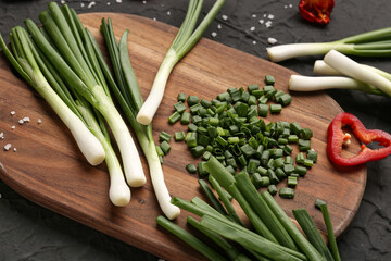 Board with slices of fresh green onion and pepper on black background