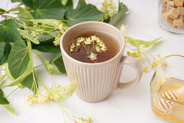 Cup of linden tea and bowl with honey on white table