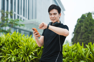 Portrait of young Asian man wearing gym clothes and using phone outside