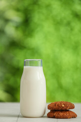 Bottle of fresh milk and sweet cookies on white tile table outdoors