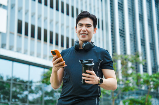 Portrait of young Asian man wearing gym clothes and using phone outside