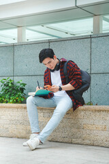 Image of young Asian male student studying and using phone on the street