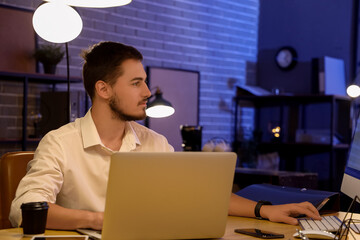 Handsome young man working with computer and laptop in office at night