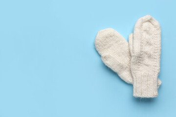 Pair of warm knitted mittens on blue background