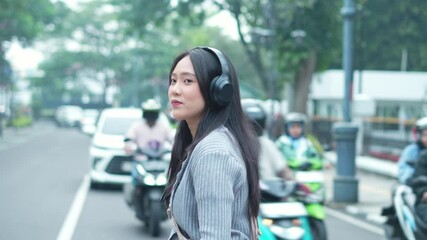 Tracking Shot Video Of Young Asian Woman Wearing Headphones Walking Cross The Street In The City - Powered by Adobe