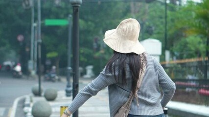 Rear View Of Young Asian Tourist Female Wear Straw Hat And Sunglasses Hailing A Taxi In The Street