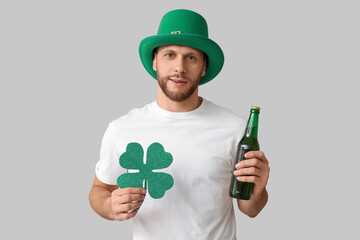 Young man in leprechaun hat with bottle of beer and clover on grey background. St. Patrick's Day...
