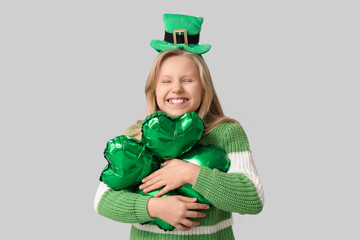 Cute little girl in leprechaun hat with air balloon in shape of clover on grey background. St....