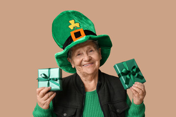 Senior woman in leprechaun hat with gift boxes on brown background. St. Patrick's Day celebration