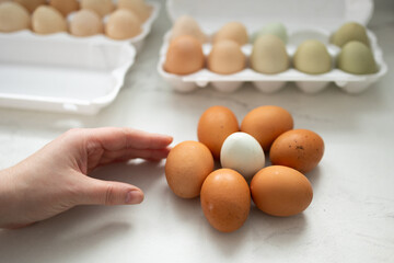 A hand is reaching for a unique and beautifully arranged collection of fresh eggs displayed on a light counter