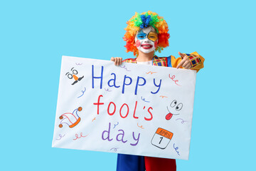Funny little boy in clown costume pointing at poster on blue background. April Fools' Day celebration