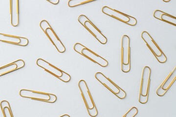 Golden paper clips on light background, flat lay