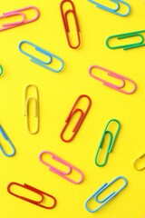 Colorful paper clips on yellow background, flat lay