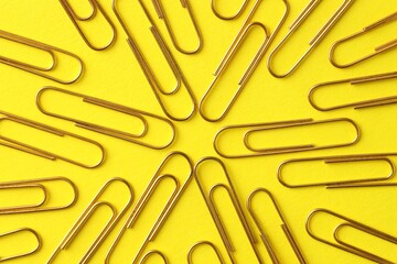 Golden paper clips on yellow background, flat lay