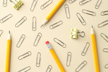Paper clips and pencils on beige background, flat lay