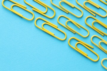 Many paper clips on light blue background, flat lay. Space for text