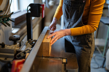 Woman carpenter hands operating electric planer, preparing and cutting wooden beams for future furniture. Woodshop production and craftswomanship, female work with precision and dedication to woodwork