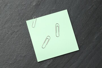 Paper note and clips on black table, top view