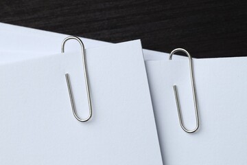 Paper notes with metal clips on black wooden table, top view