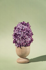 Easter egg made of lilac spring flowers in pastel green background. Sustainable holiday...